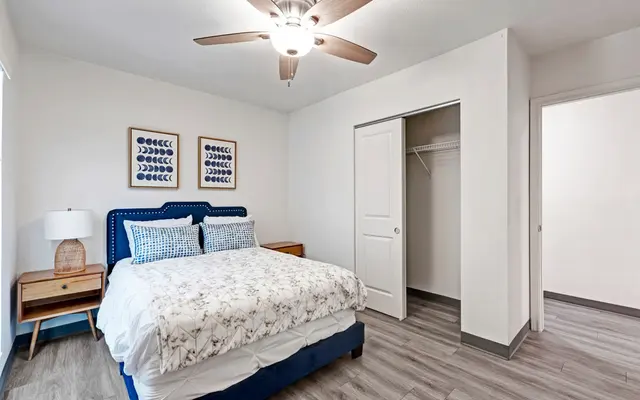 Stylish Modern Bedroom A modern bedroom featuring a double bed with a floral patterned comforter, two decorative pillows, a wooden nightstand with a lamp, and wall art with blue patterns. It includes a closet with sliding doors and light-colored wood-like flooring.
