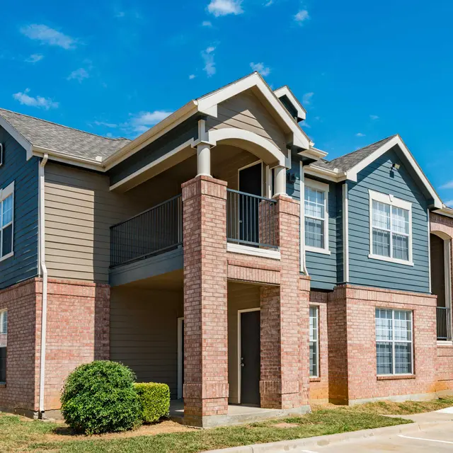 A modern two-story apartment building with a combination of brick and siding exterior under a clear blue sky.