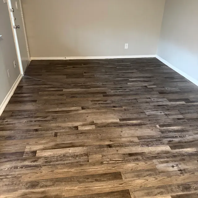 An empty room featuring a hardwood floor with varying shades of brown and a plain gray wall.