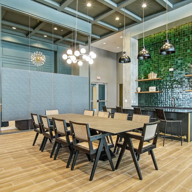 Modern common area featuring a large wooden table, stylish chairs, green tile wall, pendant lights, and contemporary decor.