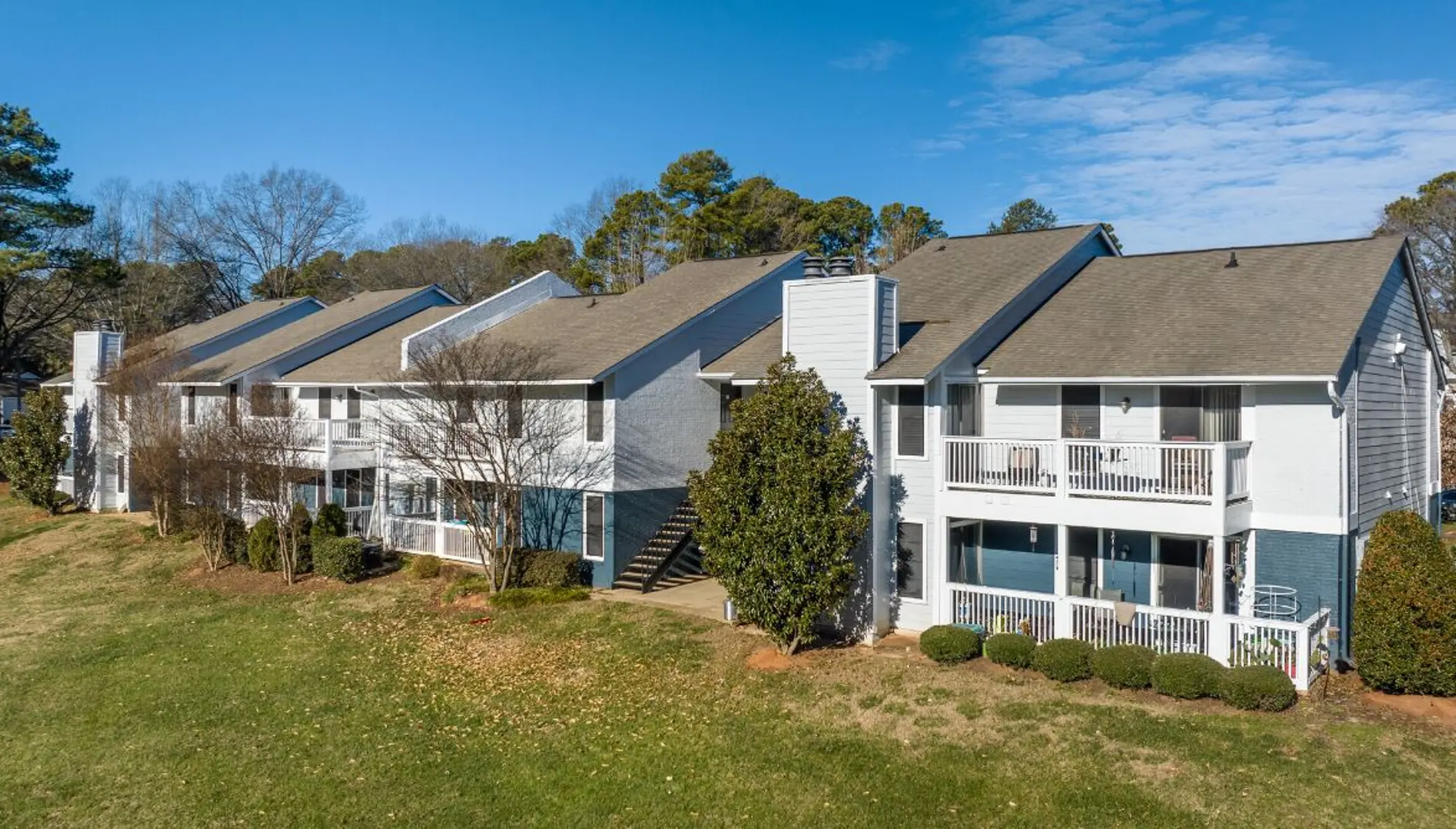 Aerial view of a multi-level apartment complex surrounded by grass and trees under a clear blue sky.