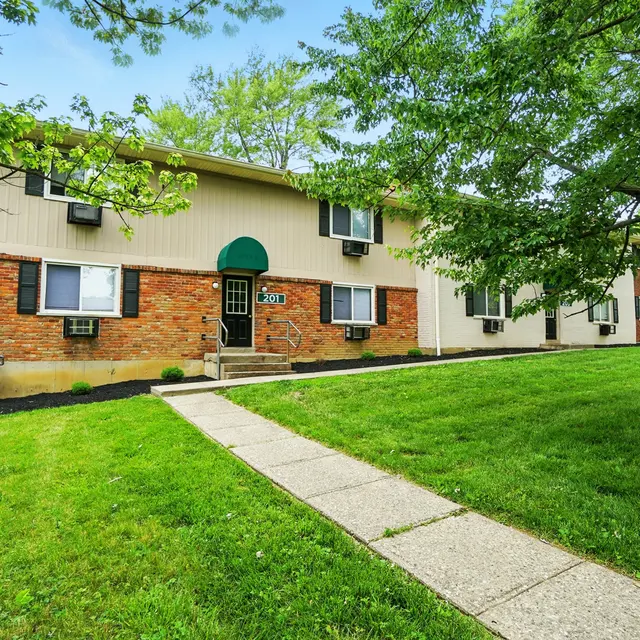 Exterior view of a residential apartment building with lush green grass and trees surrounding it.