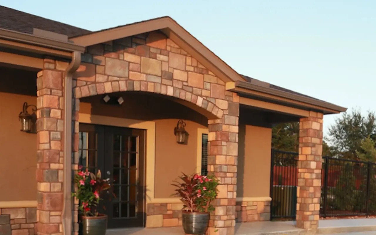 Exterior view of a building featuring a stone archway and planters with plants on either side of the entrance.