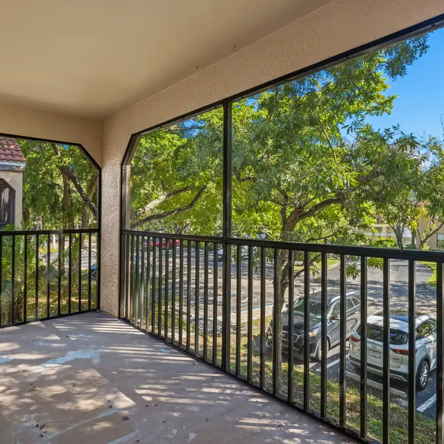 View from a balcony with black railings overlooking a parking area and trees outside.