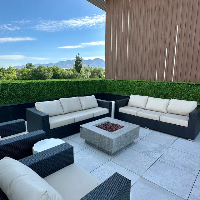 Stylish outdoor lounge area featuring cream-colored sofas, a fire pit, and a hedge backdrop, with mountains visible in the distance.