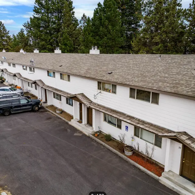 Aerial view of a townhouse complex with several linked units, parking spaces, and surrounded by trees.