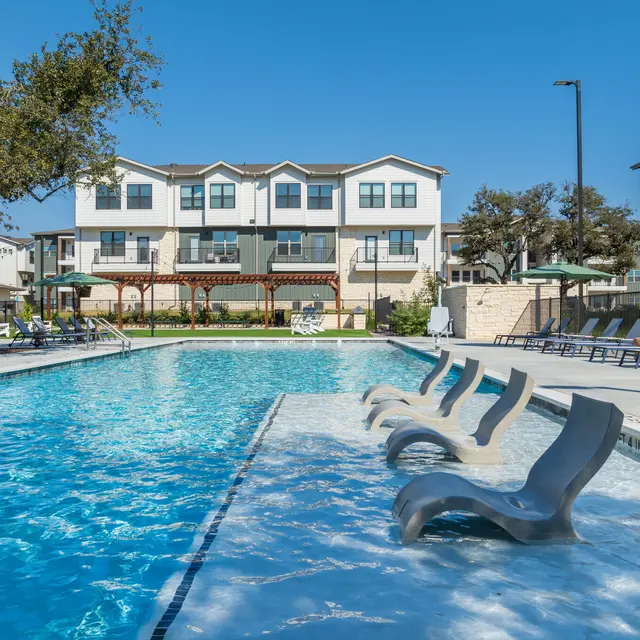 A serene swimming pool area with lounge chairs and buildings in the background on a sunny day.