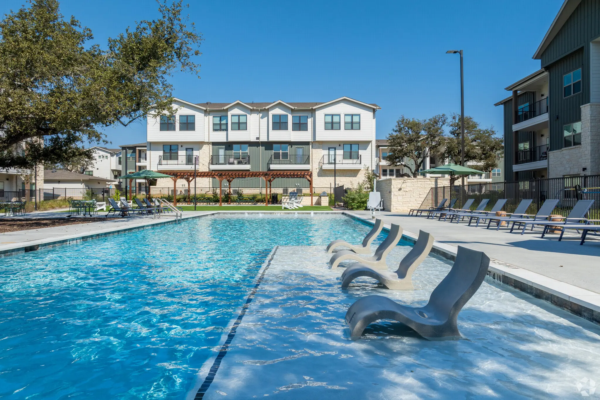 A serene swimming pool area with lounge chairs and buildings in the background on a sunny day.