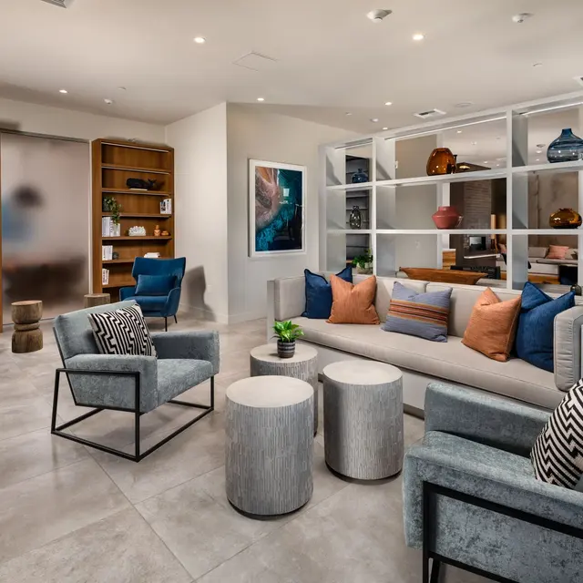 Contemporary Living Room Design A contemporary living room featuring a mix of seating, including two blue armchairs, a small table, and a sofa with colorful pillows. There are shelves with decorative items in the background and a plant in one corner.