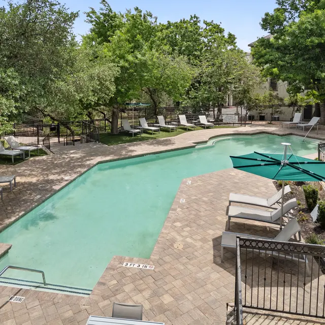 A serene swimming pool area featuring a rectangular pool surrounded by lounge chairs and green trees.