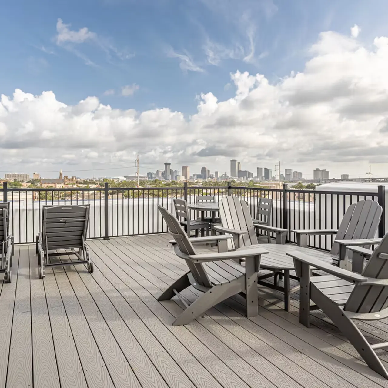 A spacious rooftop deck featuring wooden chairs and tables overlooking a city skyline under a partly cloudy sky.