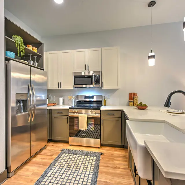 Modern Kitchen Interior A modern kitchen featuring stainless steel appliances, white cabinetry, and a large sink. The design includes wood flooring, a patterned rug, and two pendant lights hanging from the ceiling.