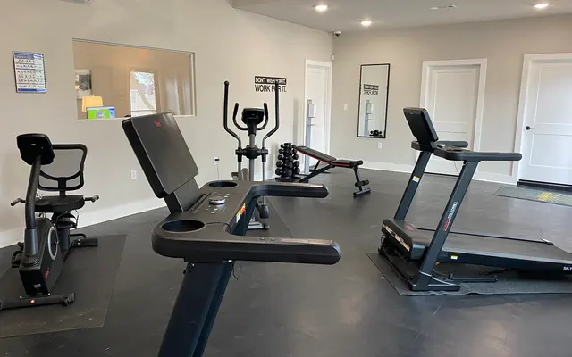 Interior of a modern gym with various fitness equipment including treadmills, an elliptical machine, and stationary bikes.