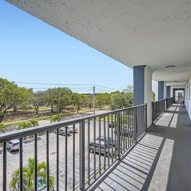 A view from a balcony overlooking a parking lot and green trees in the background under a clear blue sky.