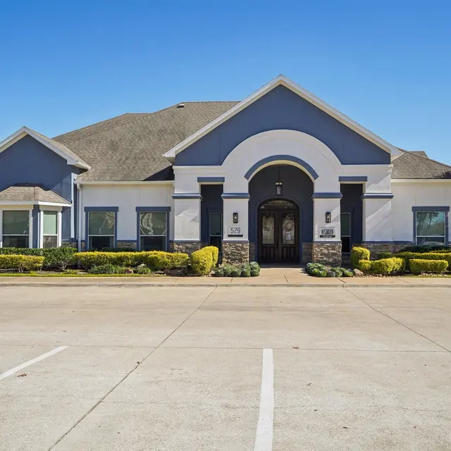 A modern residential building with a large front entrance and manicured landscaping under a clear blue sky.
