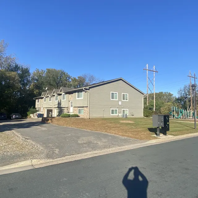 View of an apartment complex with a playground and utility poles in the background under a clear blue sky.