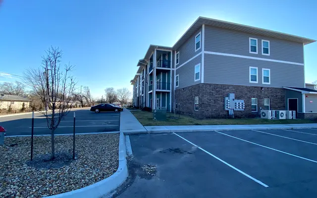 Side view of a modern apartment complex with a parking lot in the foreground and clear blue sky.