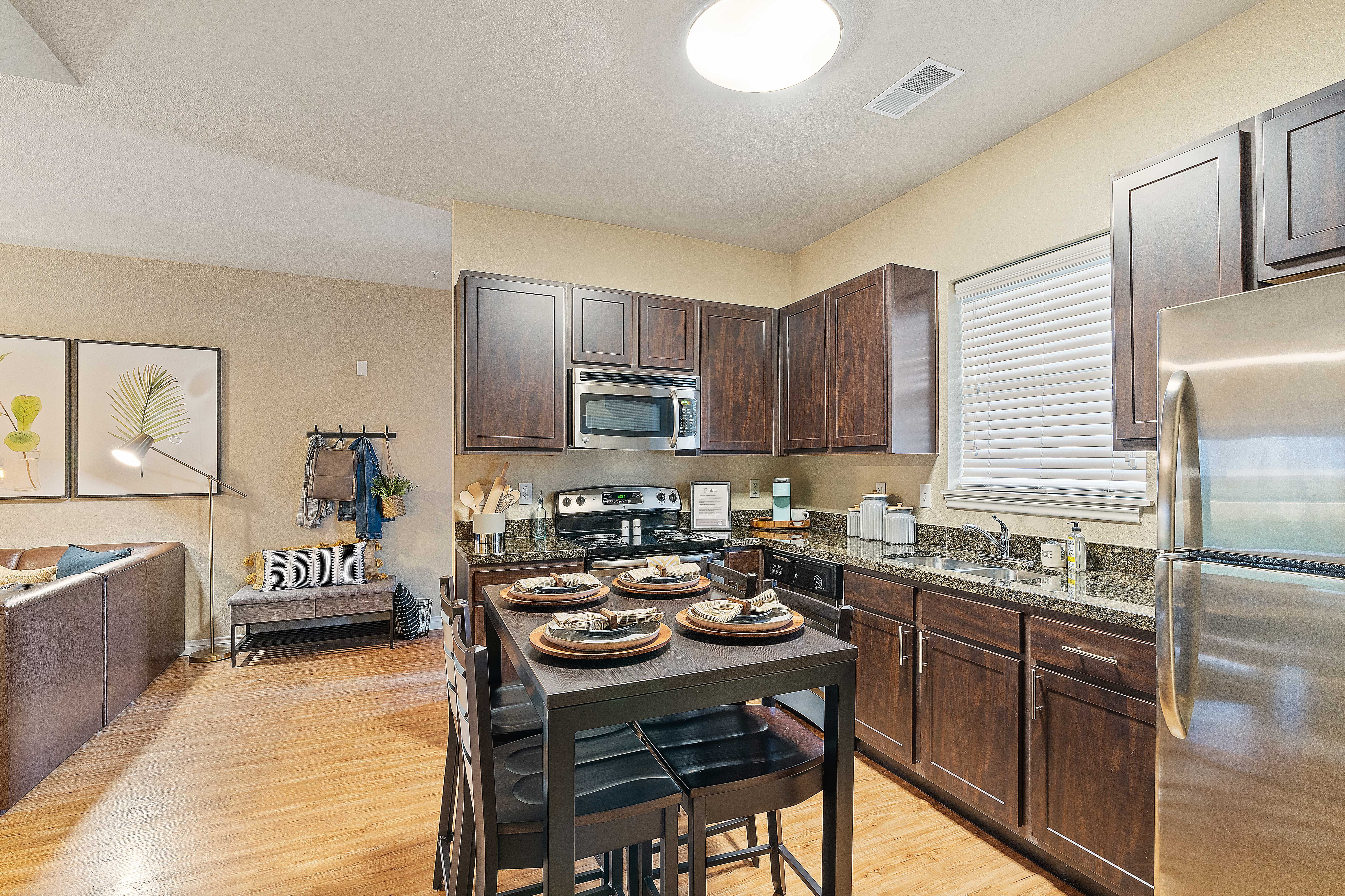 A modern kitchen featuring dark wooden cabinets, stainless steel appliances, and a dining table set for four with plates and utensils.