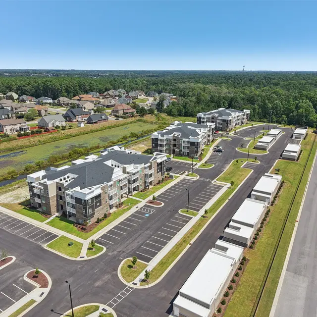 Aerial view of a modern apartment complex surrounded by vacant parking lots and residential homes.