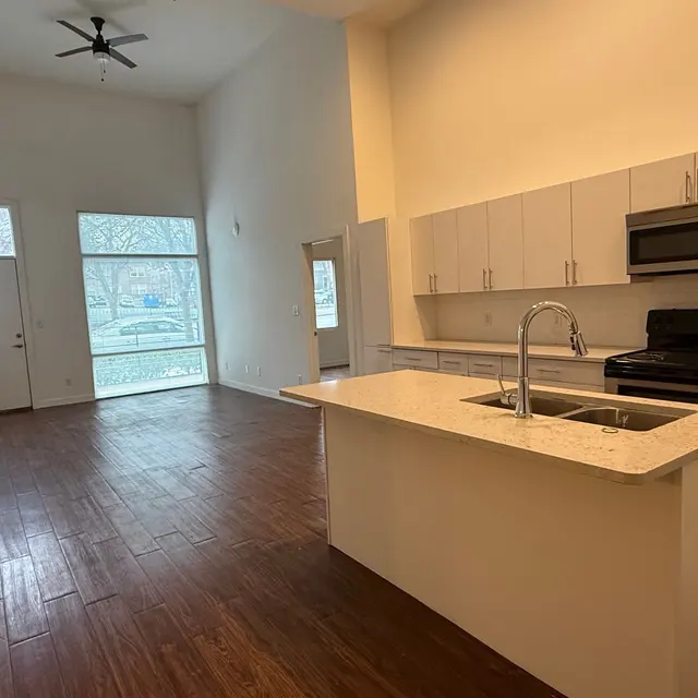 A modern kitchen and living area with wood flooring, high ceilings, and large windows allowing natural light.