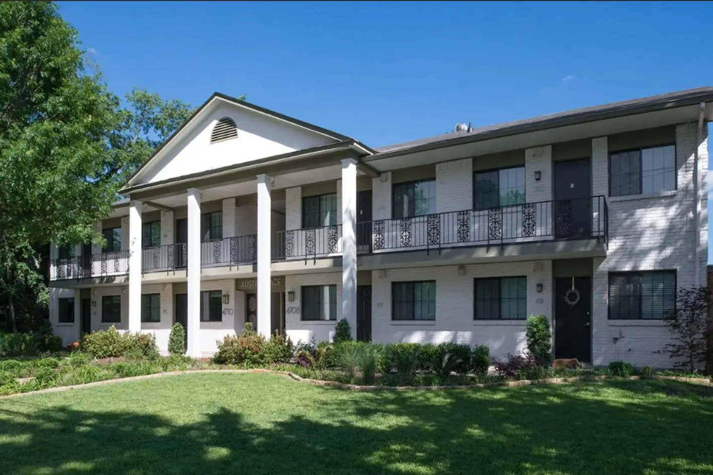 Exterior view of a two-story apartment building with white walls and a green lawn.