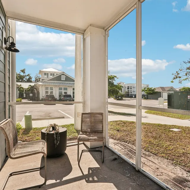 Screened-In Porch View A screened-in porch with two chairs and a small table, looking out toward a parking lot and nearby houses.