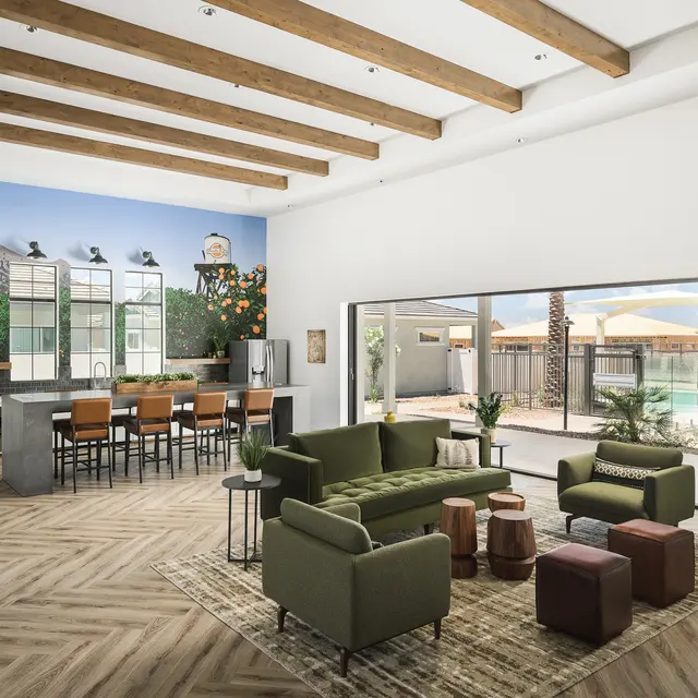 A spacious modern living area featuring a green sofa set, wooden beams on the ceiling, a mural of an orange tree and mountains, and a pool view through large windows.