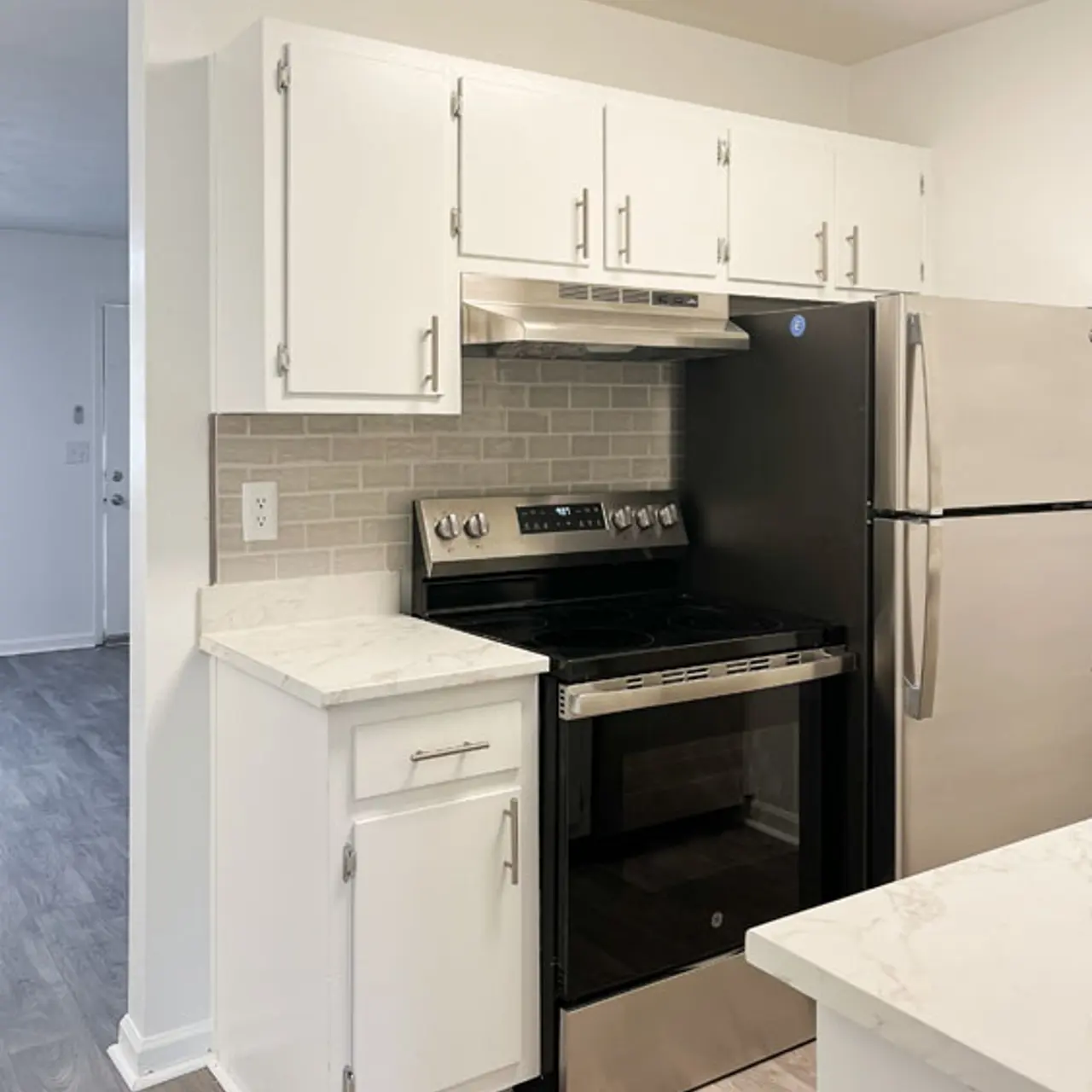 A modern kitchen featuring white cabinets, a black stove, stainless steel refrigerator, and a light gray tiled backsplash.