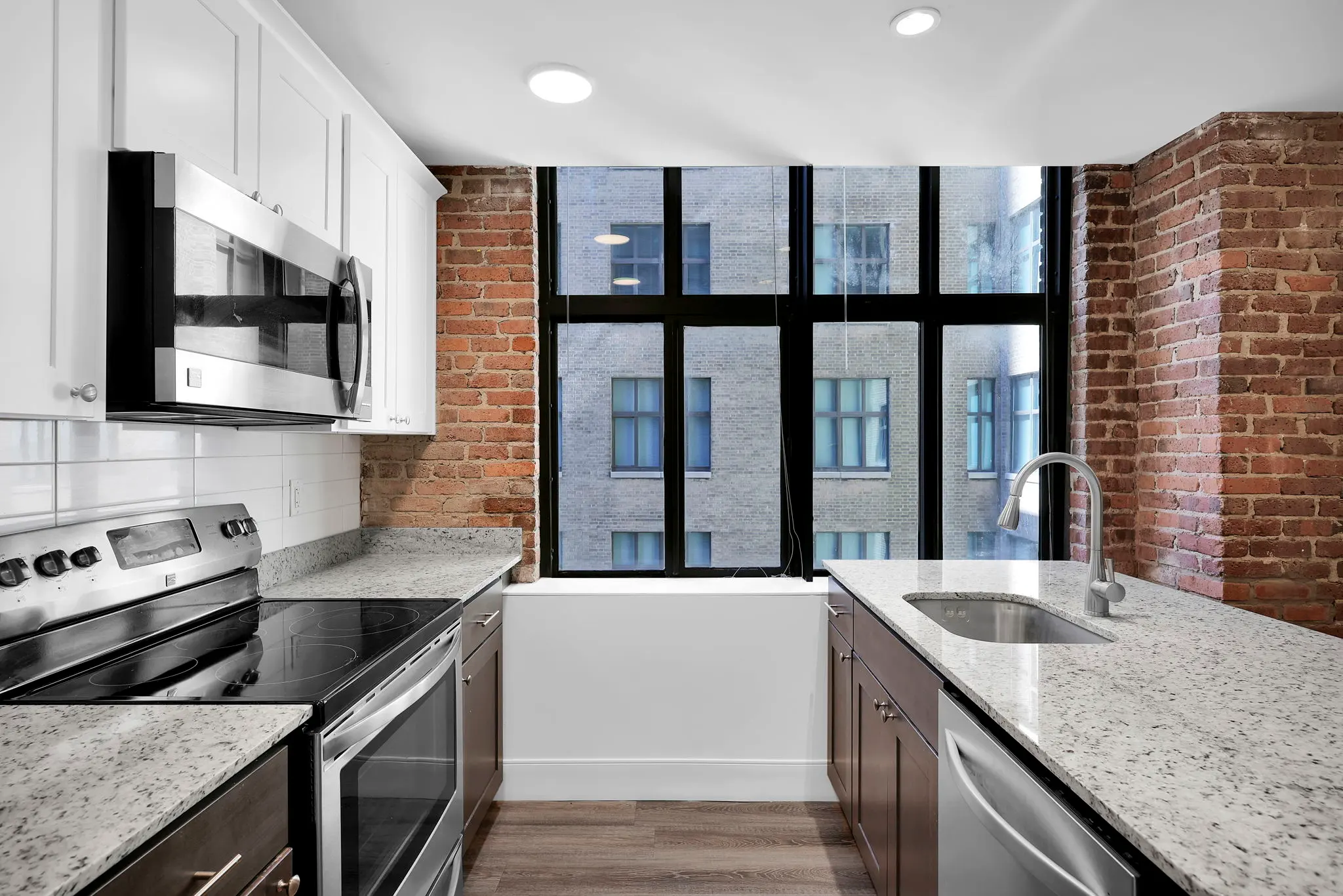 A modern kitchen featuring stainless steel appliances, granite countertops, and large windows with an urban view.