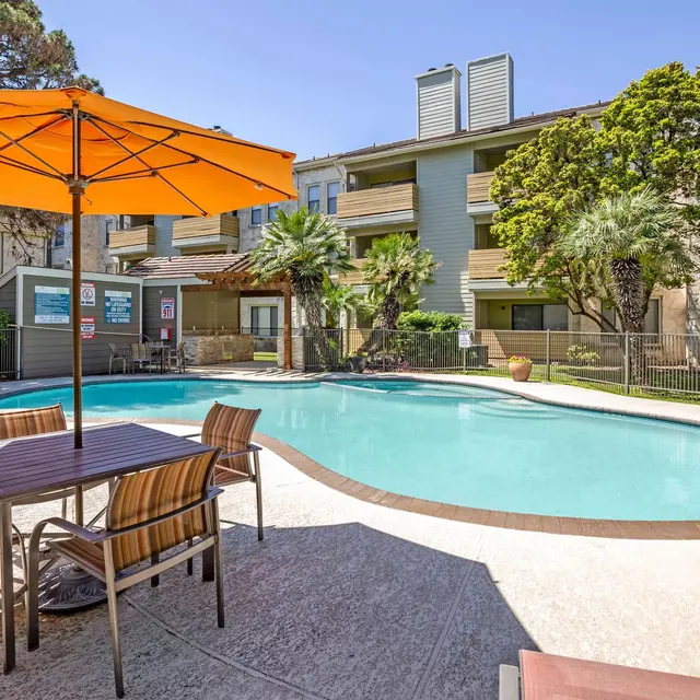 Outdoor swimming pool area featuring lounge chairs and an orange umbrella near the pool.