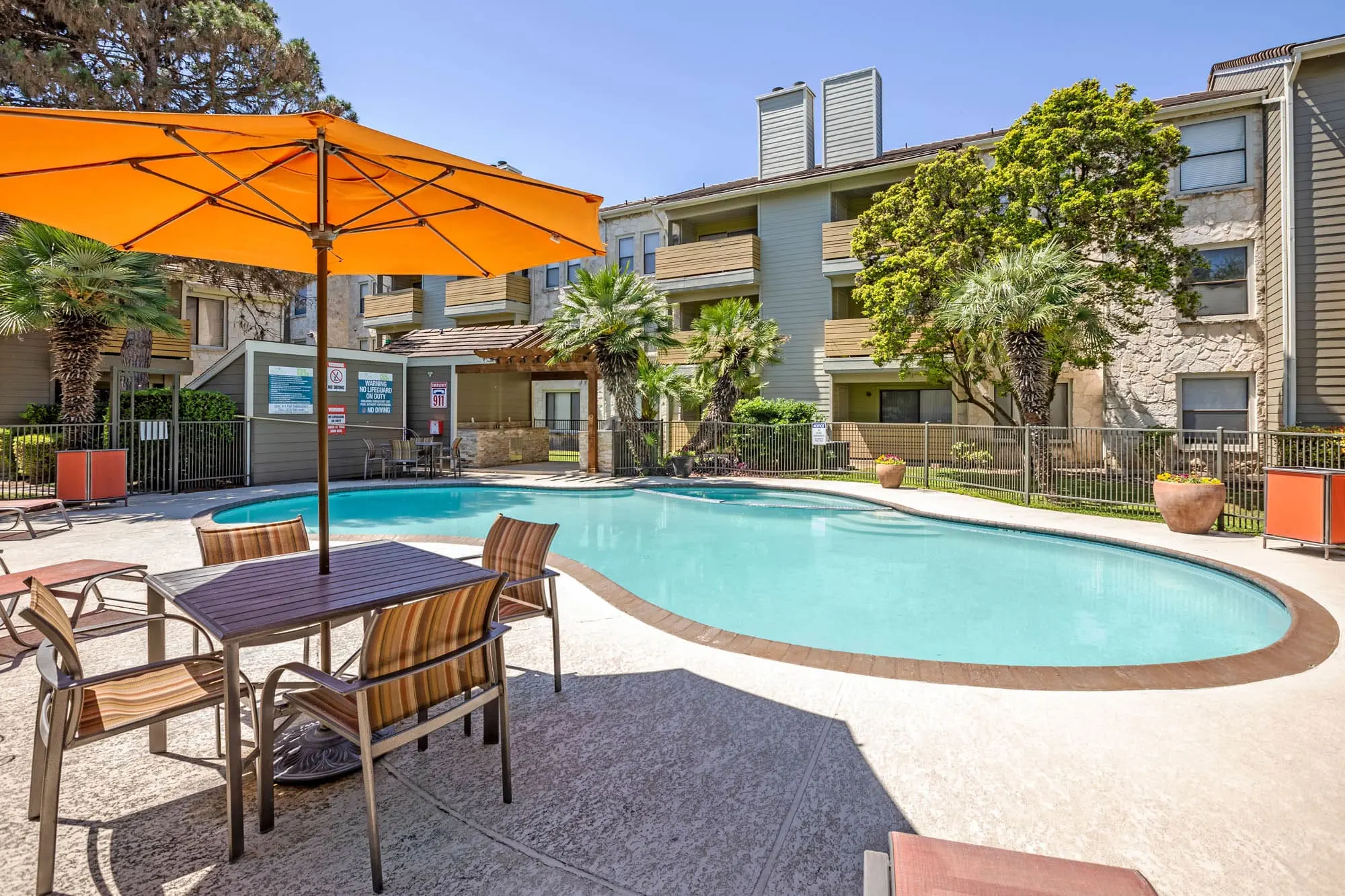 Outdoor swimming pool area featuring lounge chairs and an orange umbrella near the pool.
