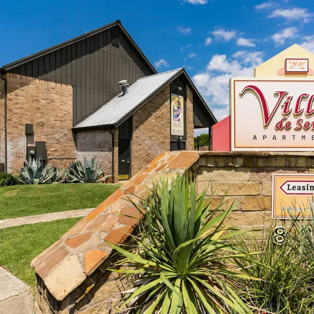 Exterior view of the Villas de Sendero Apartments featuring a leasing center sign and landscaped area.