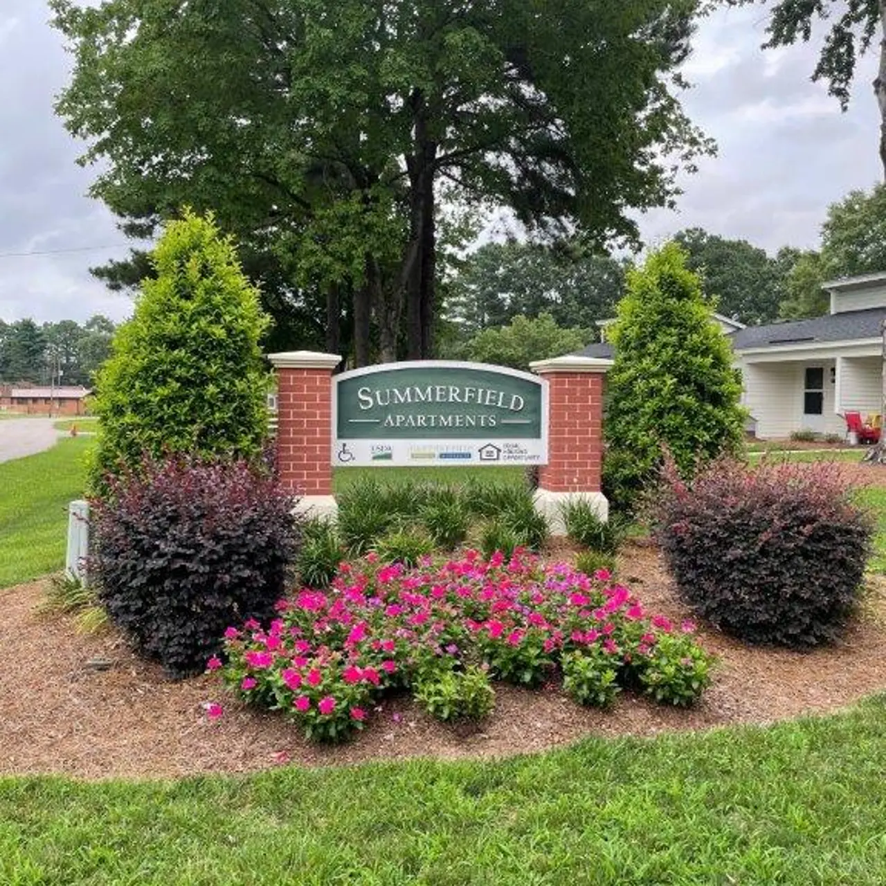 Sign for Summerfield Apartments surrounded by colorful flowers and green shrubs.