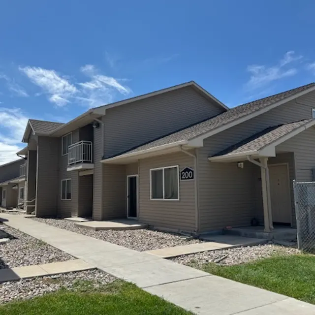 Two-story apartment buildings with a sidewalk and grassy area in front.