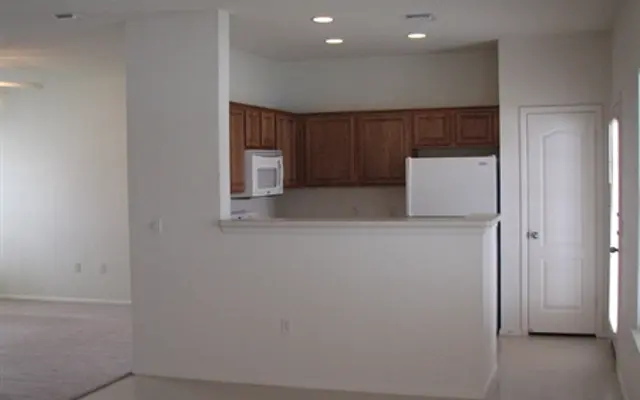 Open Concept Kitchen and Living Room An open-concept kitchen and living room area with light-colored walls and cabinets, and a door leading outside.