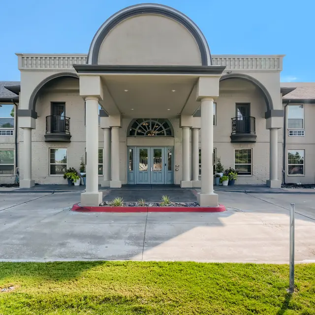 Front view of a modern hotel building with a large arch entrance, columns, and balconies on the upper floor.