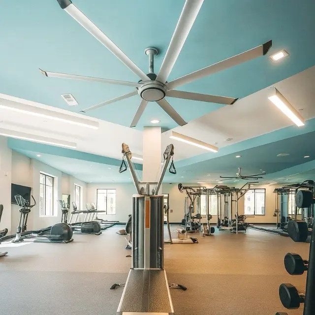 Interior view of a modern gym featuring a large ceiling fan, exercise equipment, and natural light coming through windows.