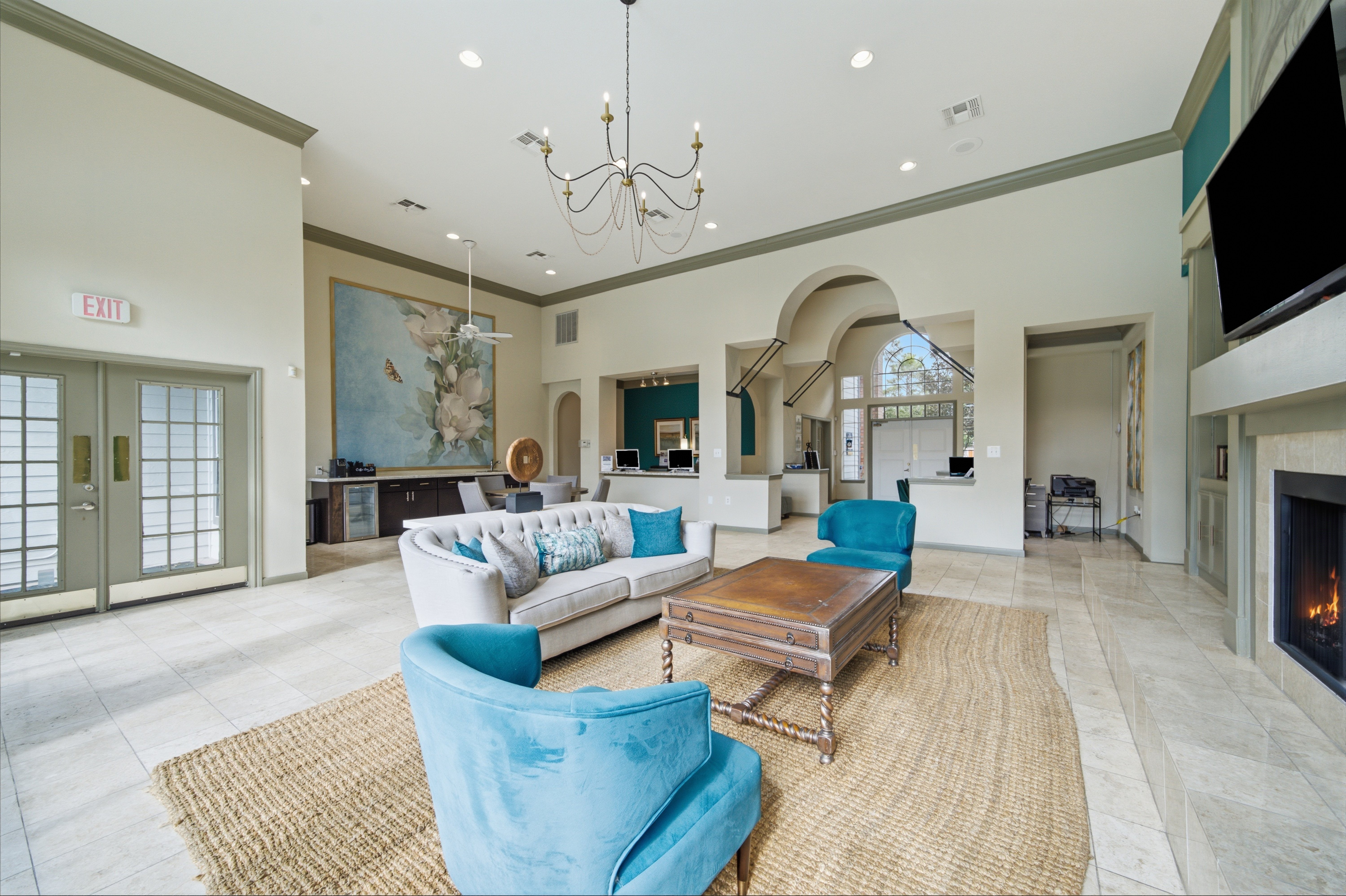 A spacious community lounge with elegant decor, featuring comfortable seating, a coffee table, and a fireplace, along with a large mural on the wall and windows letting in natural light.