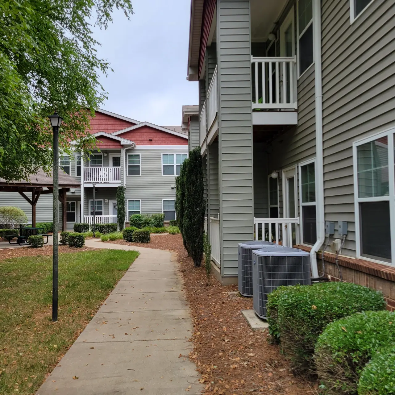 Pathway leading through an apartment complex with greenery and buildings on either side.