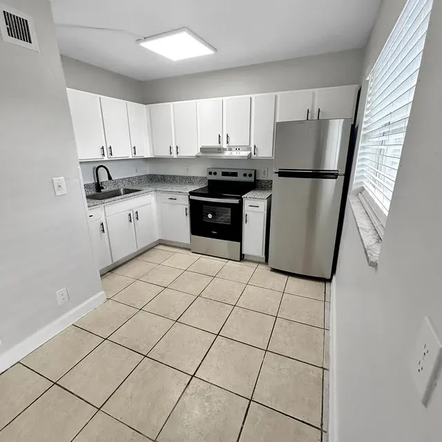 A clean and modern kitchen with white cabinets, stainless steel appliances, and tiled floor.