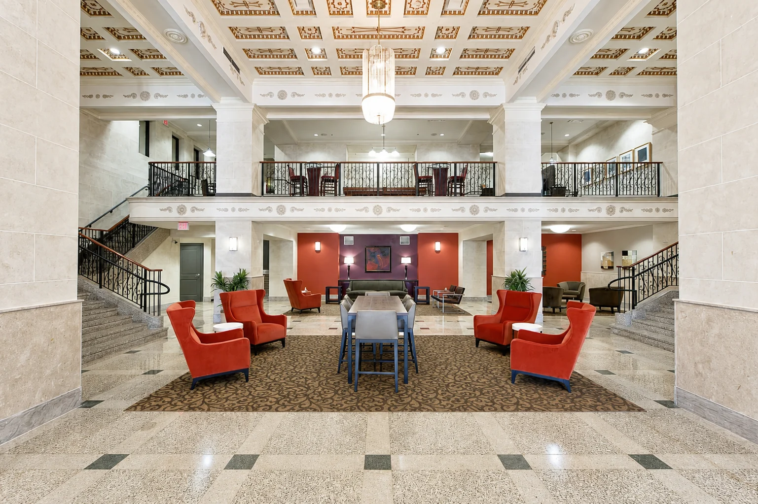 A spacious lobby area featuring red chairs, a central table, and decorative elements on the ceiling and walls.