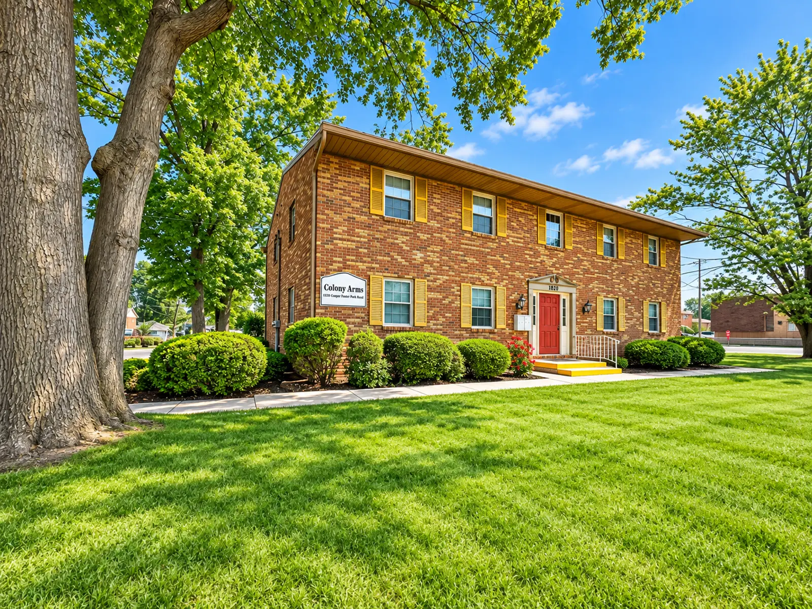 A brick apartment building surrounded by well-manicured grass and trees under a clear blue sky.