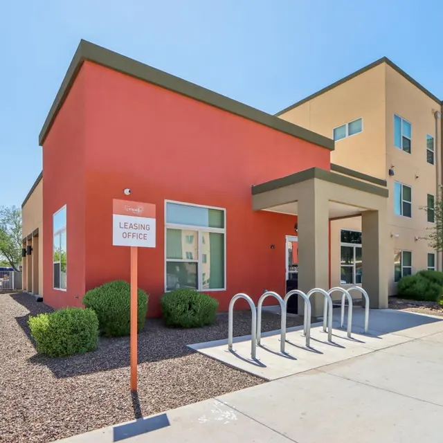 Exterior view of a leasing office building with a red facade and bicycle racks in front.