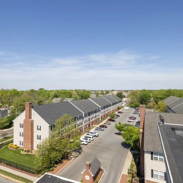 A sunny overhead view of a residential neighborhood showing rows of buildings and green trees lining the streets.