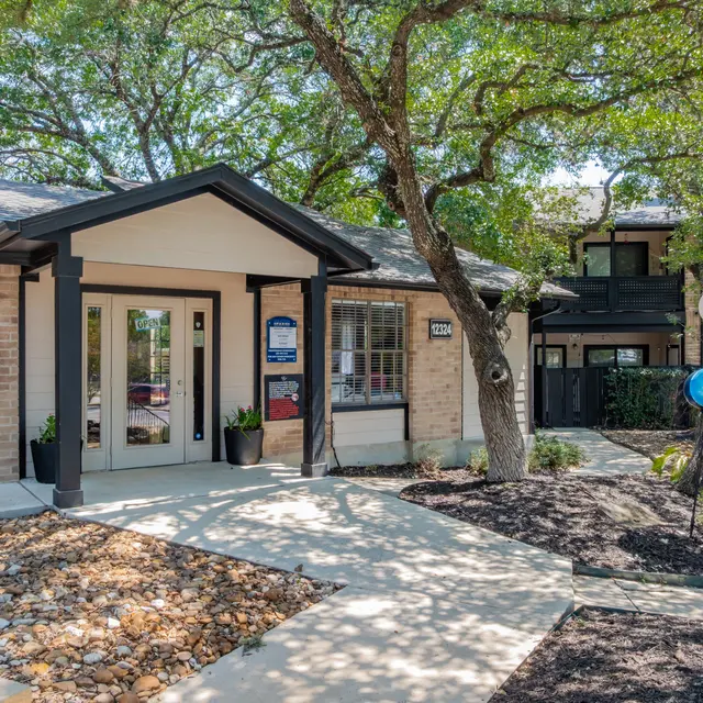 View of an apartment complex entrance surrounded by trees, with a path leading to the main door.