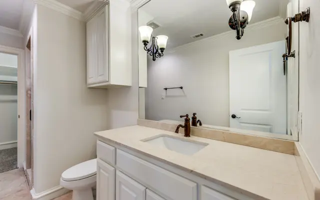 Modern Bathroom Interior A modern bathroom with white cabinetry, a light-colored countertop, and a mirror above the sink. Features sconces on either side of the mirror and a door leading to a closet area in the background.