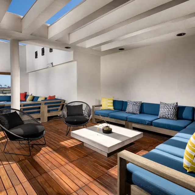 Stylish Outdoor Lounge Area Stylish outdoor lounge area featuring a spacious wooden deck with comfortable blue seating and decorative cushions, complemented by modern chairs and a central coffee table.