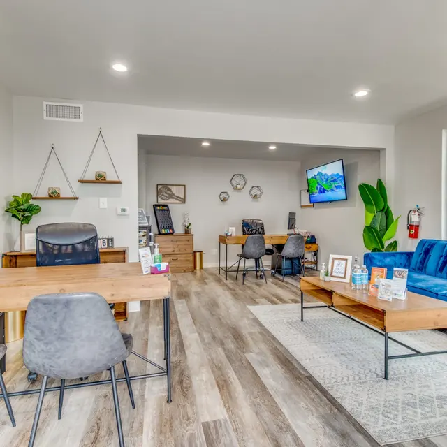 A modern office interior featuring a blue couch, wooden desks, and a display screen on the wall.