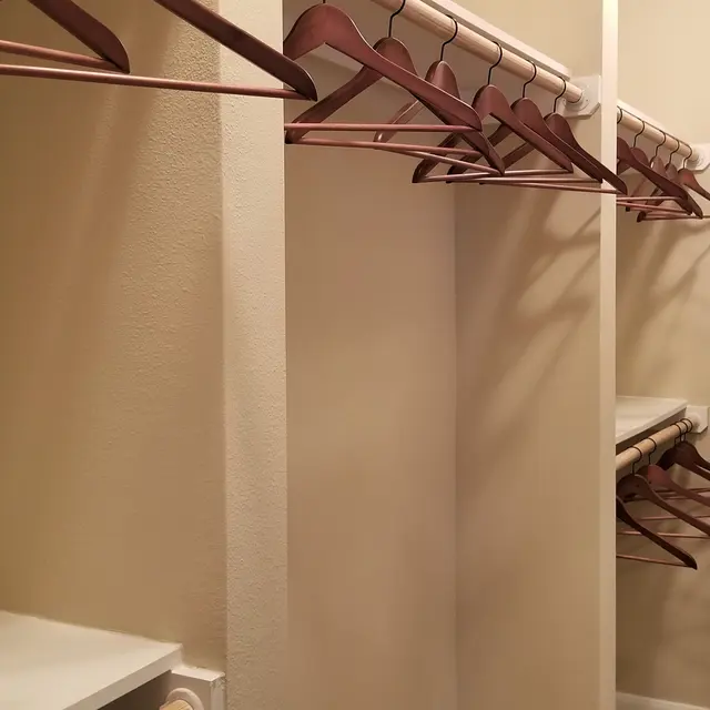 A spacious closet with beige walls, featuring multiple rows of wooden hangers, a shelf, and neatly rolled towels.