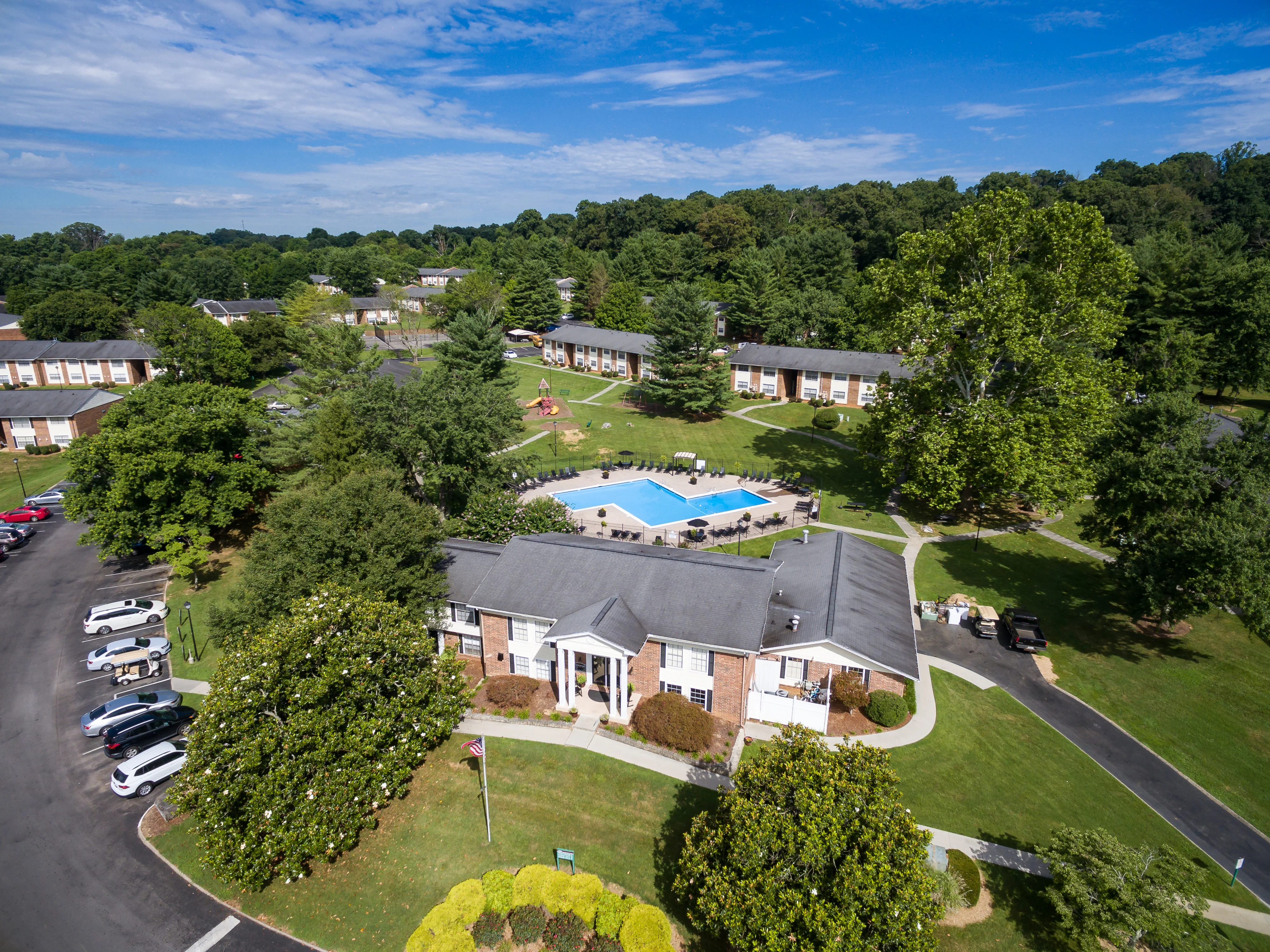 Aerial view of a residential apartment complex featuring a swimming pool, surrounded by landscaped greenery and parking areas.
